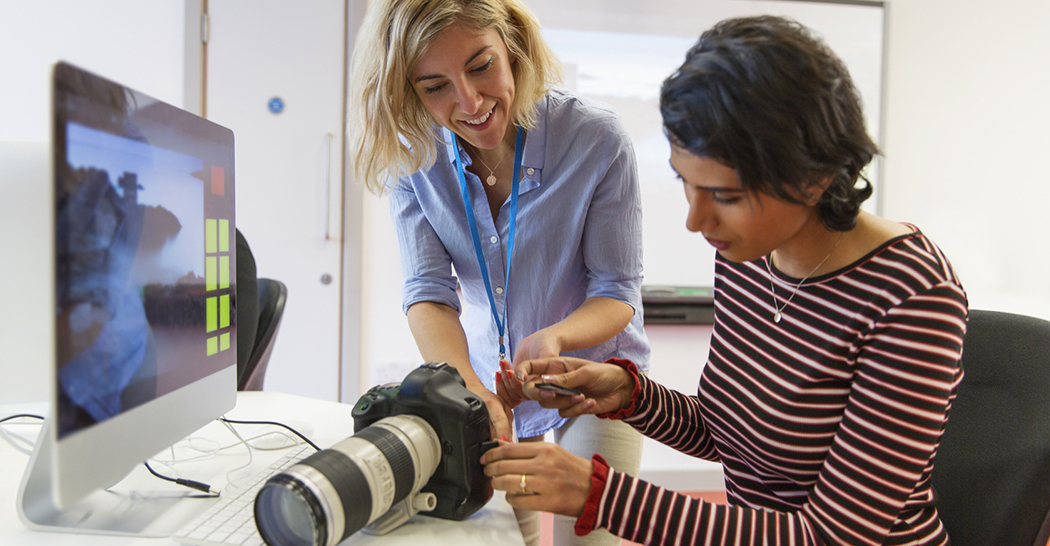 Professora ajuda aluna a inserir placa de memória em máquina fotográfica digital profissional em laboratório de fotografia.